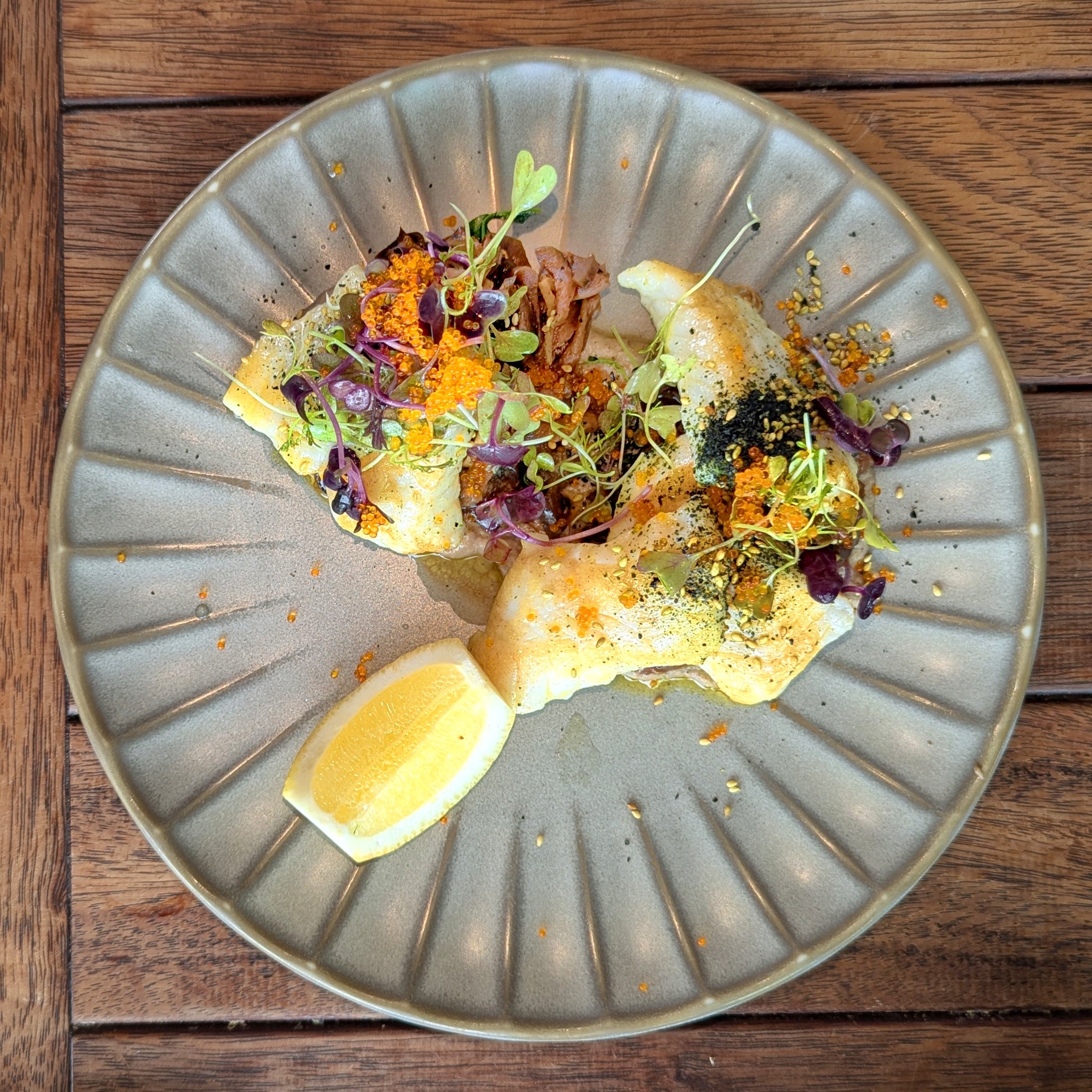 Pan-cooked cod with butter sauce, microgreens and lemon on a fluted plate