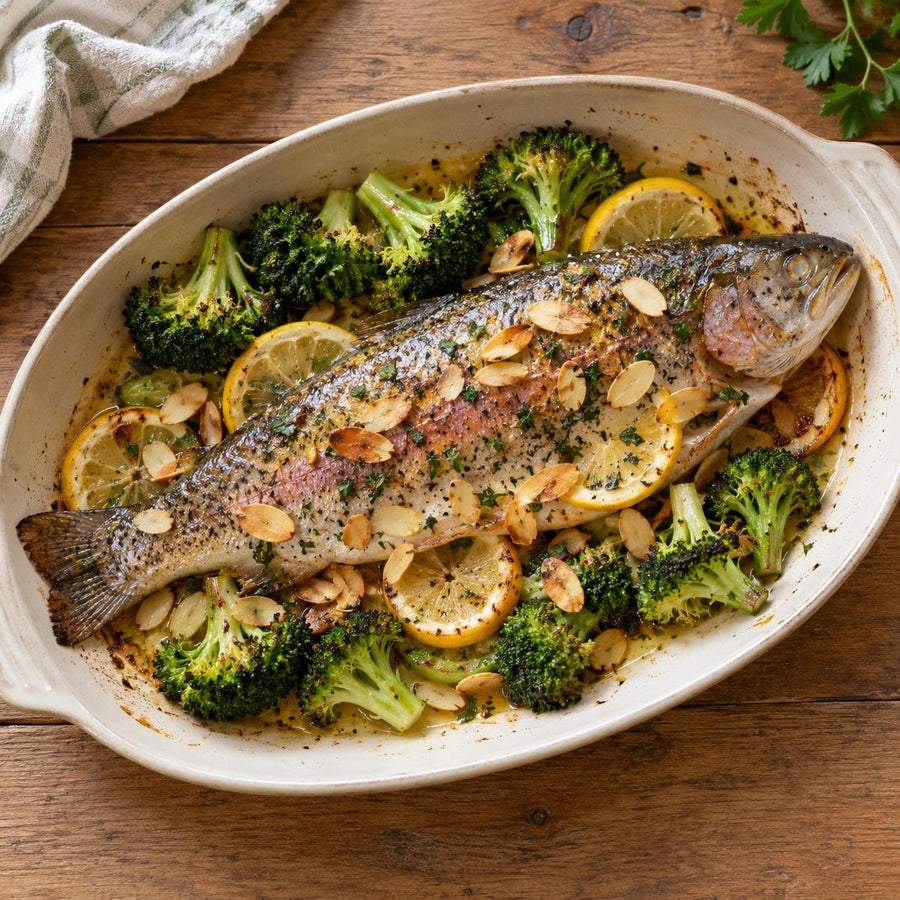 Baked whole rainbow trout with flaked almonds, lemon slices and broccoli in a cream oval dish
