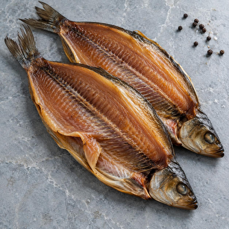 Two cold-smoked butterfly kippers on a grey stone slab with black peppercorns