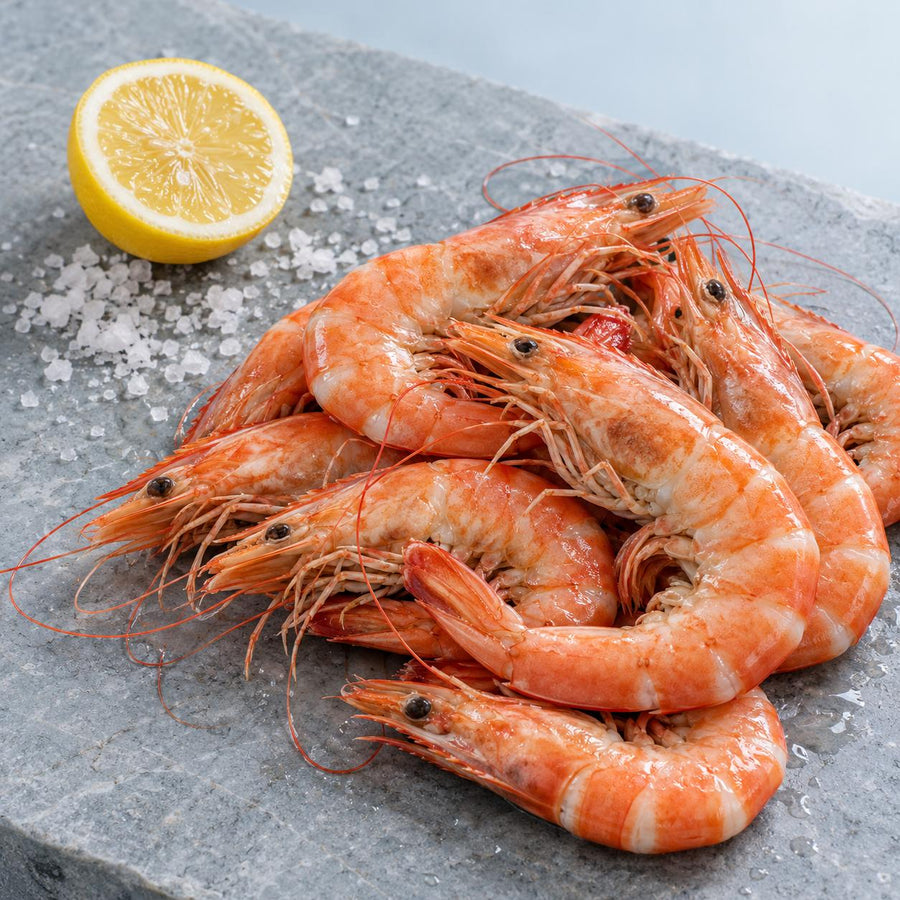 Cooked whole crevettes in the shell on a grey stone slab with half a lemon and flaked sea salt