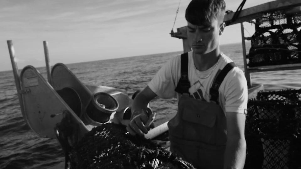 Black and white photograph of a fisherman working nets and creels on deck