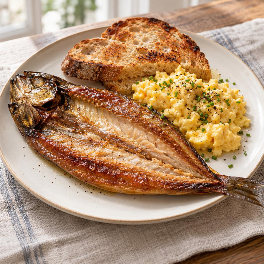 Kipper opened flat with scrambled eggs, chives and two slices of toast on a pale stoneware plate