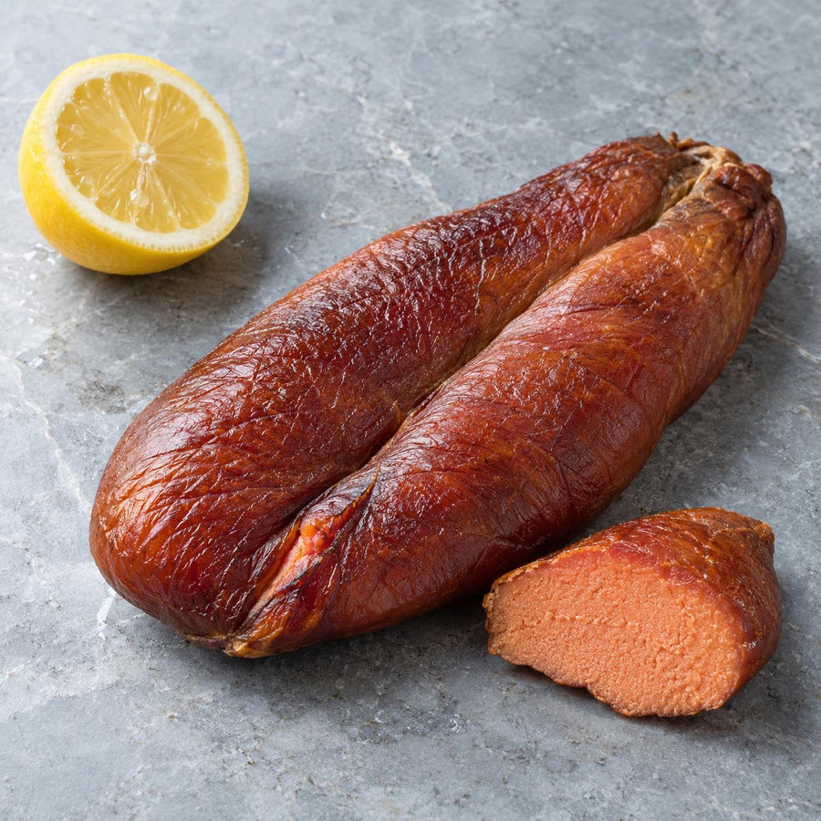 A pair of smoked cod's roe beside a cut piece on a grey stone slab with half a lemon