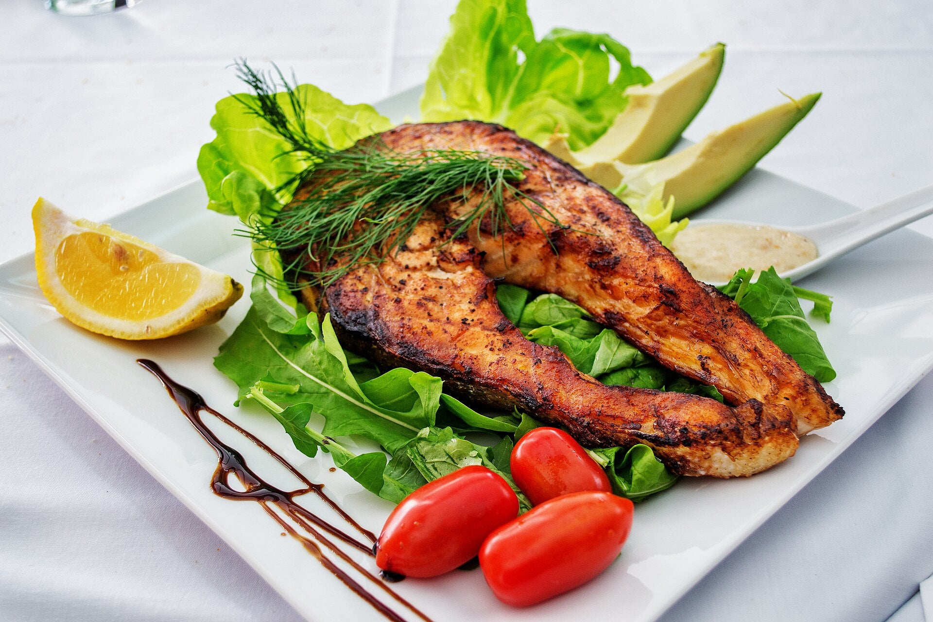Grilled salmon fillet with salad and lemon on a white plate