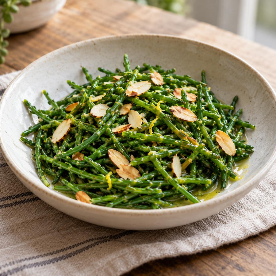Samphire tossed in butter with toasted flaked almonds and lemon zest in a pale stoneware bowl on a linen cloth
