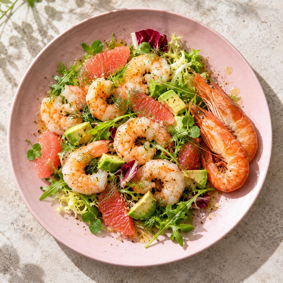 Crevettes in a salad with pink grapefruit, avocado, rocket, frisée and dill on a pale pink plate