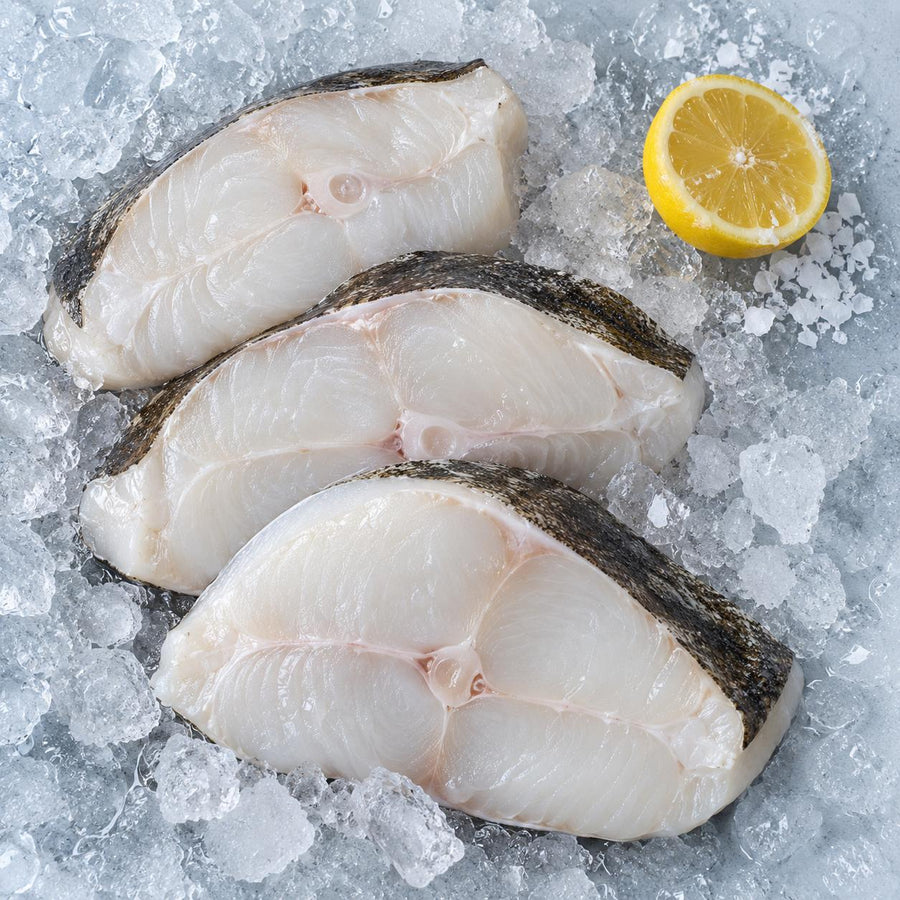 Three raw halibut steaks on crushed ice with half a lemon and sea salt
