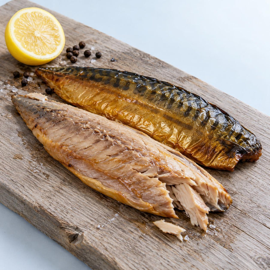 Two hot-smoked mackerel fillets on a weathered oak board with half a lemon and black peppercorns