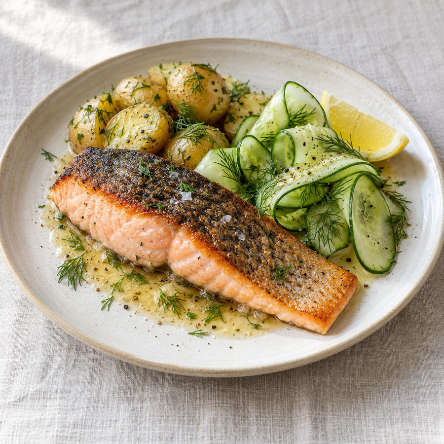 Pan-fried wild sea trout fillet with dill new potatoes, cucumber ribbons and lemon on a cream plate