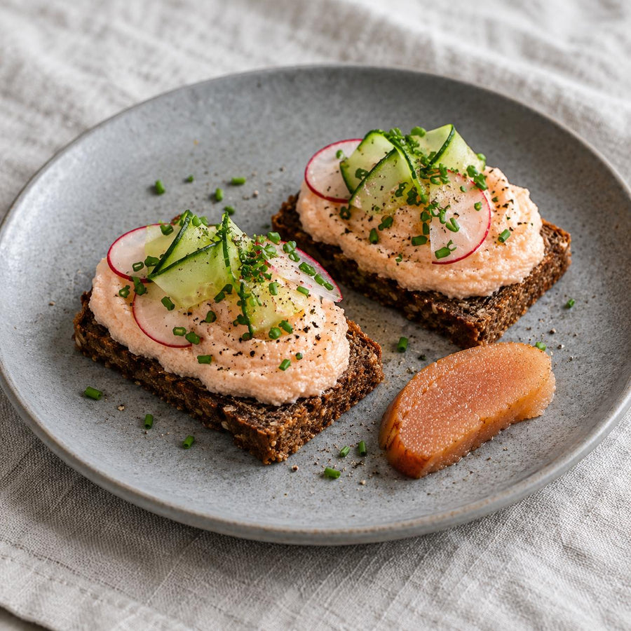 Smoked cod's roe whipped on rye toasts with radish, cucumber ribbons and chives beside a slice of roe on a grey plate